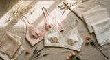 Two soft wire-free bralettes in blush and ivory tones displayed side by side on a linen surface with delicate dried flowers, bathed in warm natural light.
