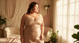 A confident plus-size woman in elegant nude lingerie stands in warm natural light by a sunlit window, exuding comfort and self-assurance.