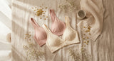 Two wireless comfort bralettes in blush and ivory tones arranged in a soft flat lay with dried flowers on a linen surface in warm natural light.