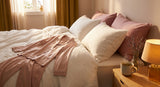 Soft golden-lit bedroom with elegant pajamas draped over white linen bedding, a cup of herbal tea, and dried lavender on a bedside table.
