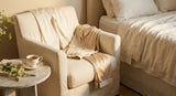 Luxurious ivory cotton pyjamas draped over a plush armchair in a softly lit, elegant bedroom setting with a cup of tea on a marble side table.